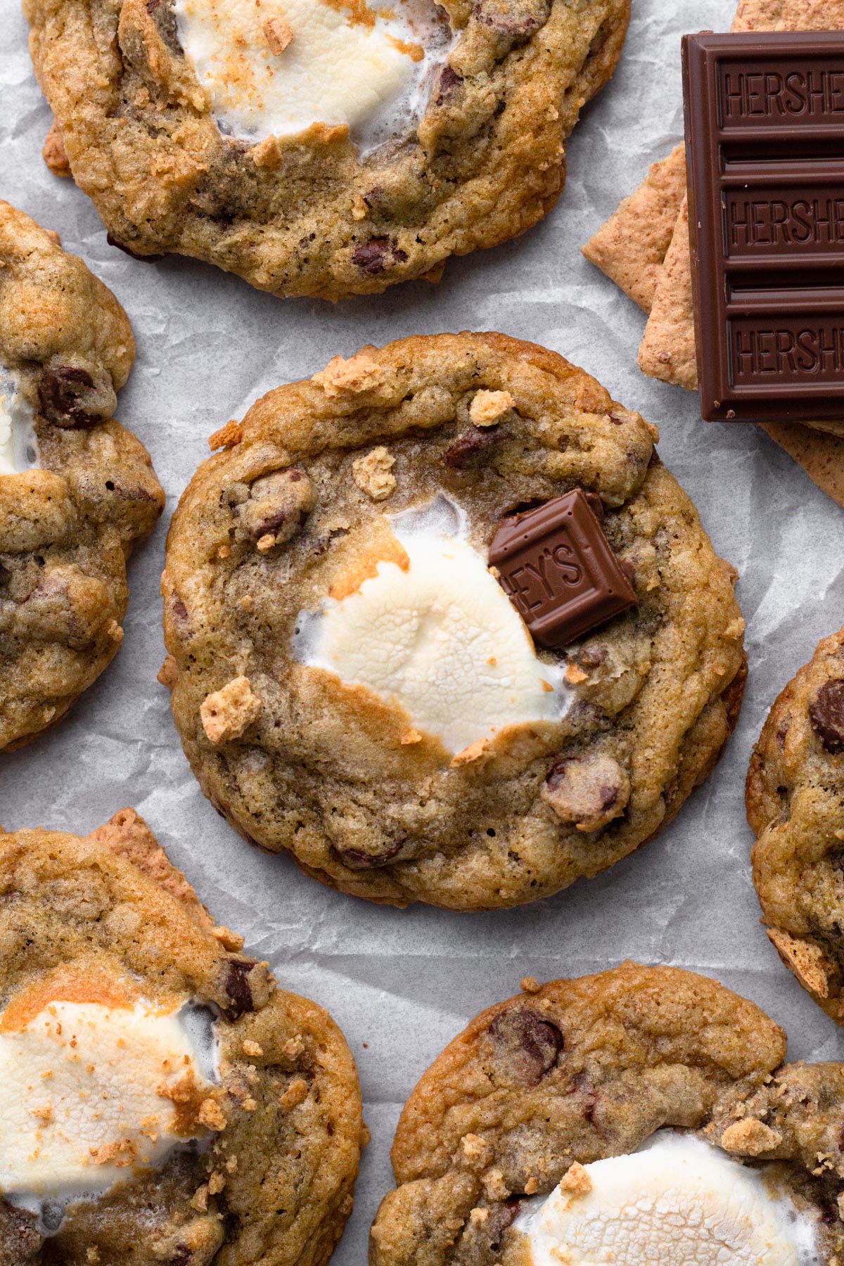 S'mores cookies with toasted marshmallow, graham cracker crumbs, and milk chocolate bar on a crinkled piece of parchment paper.
