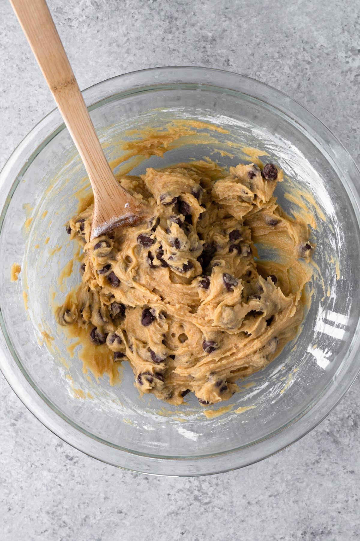 Cookie dough with chocolate chips in a glass mixing bowl with a wooden spoon.