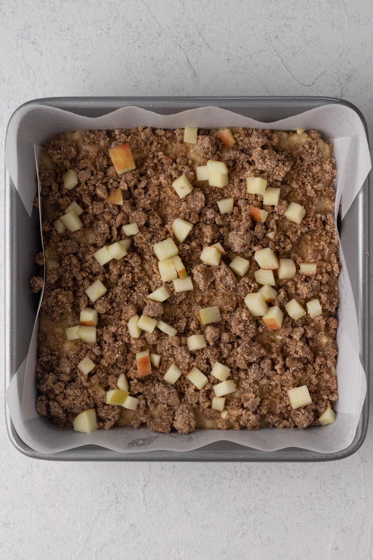 Cake batter layered with crumb filling and chopped apples in a square baking pan.