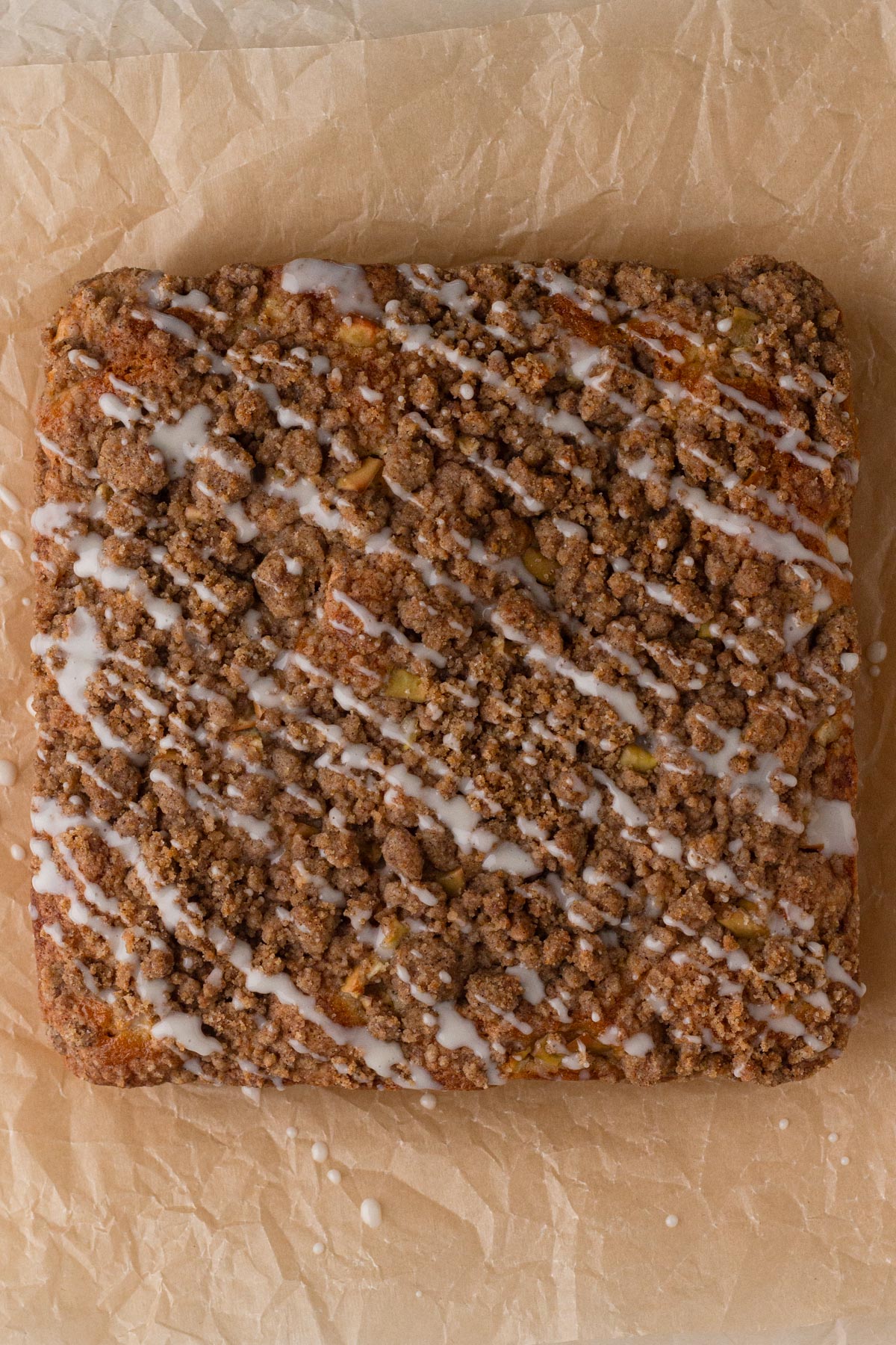 Coffee cake drizzled with white glaze on brown parchment paper.