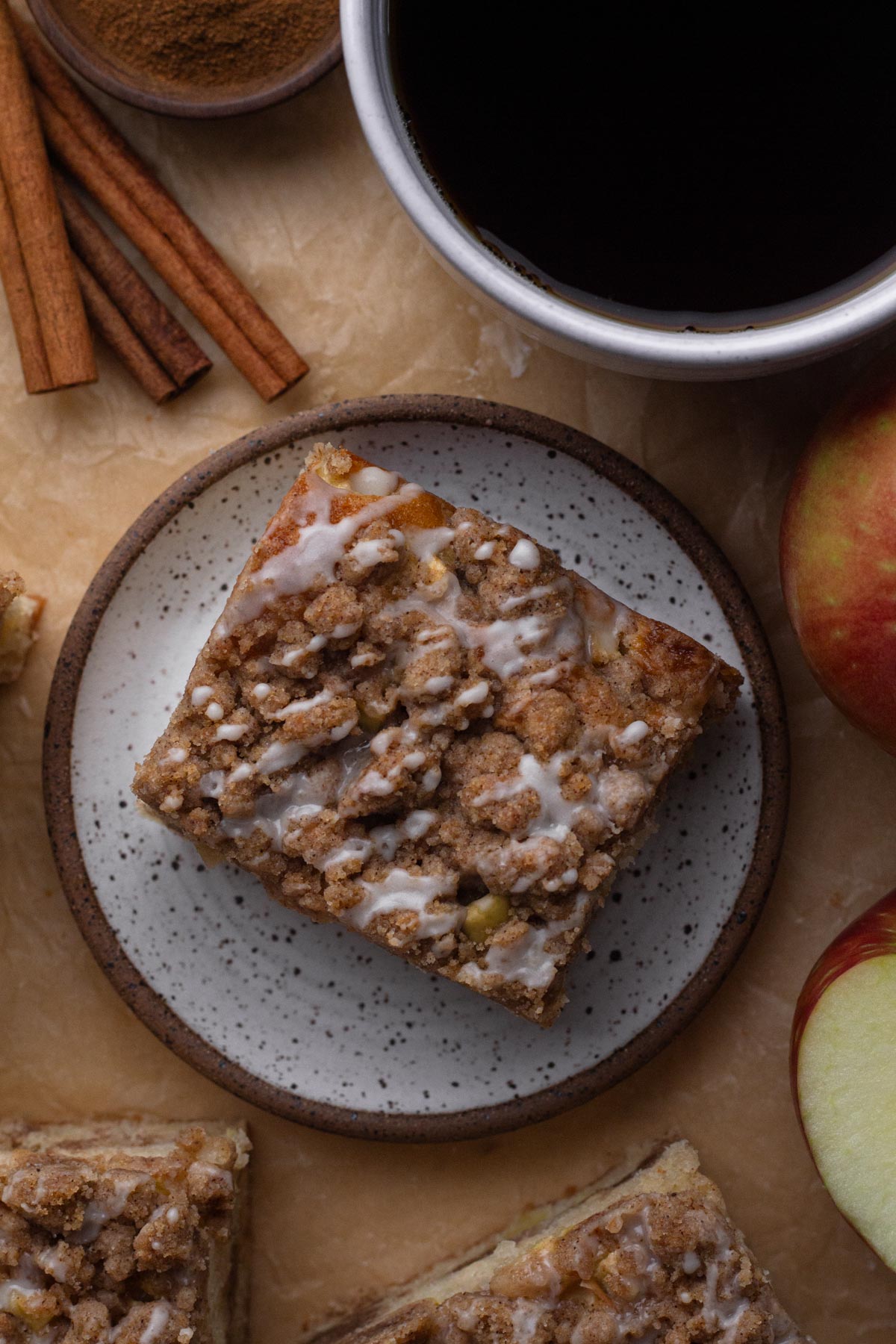 Overhead view of a slice of coffee cake topped with crumbs and a drizzle of glaze on a white plate.