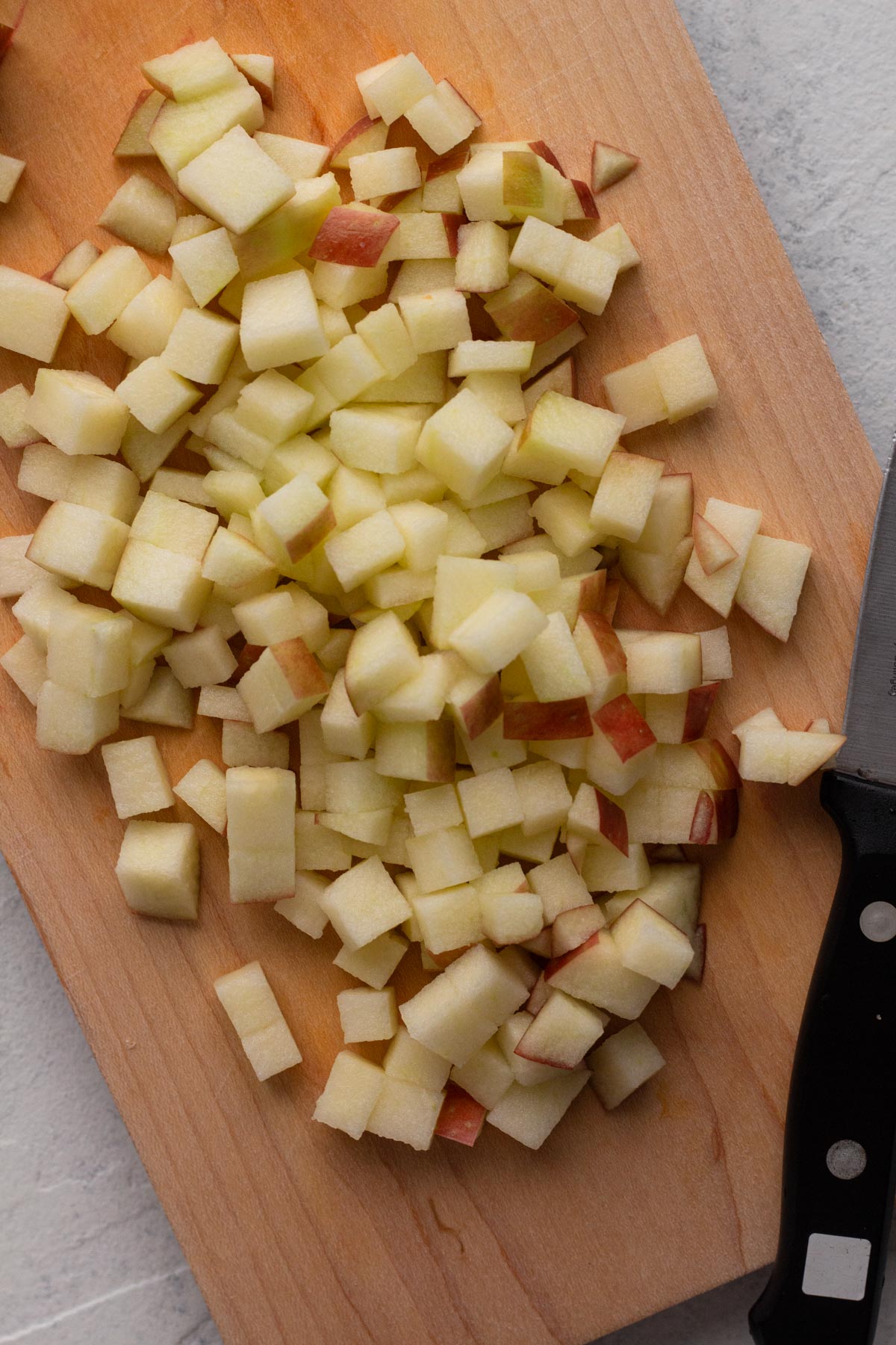 Chopped apple bits on a wooden cutting board with a knife.