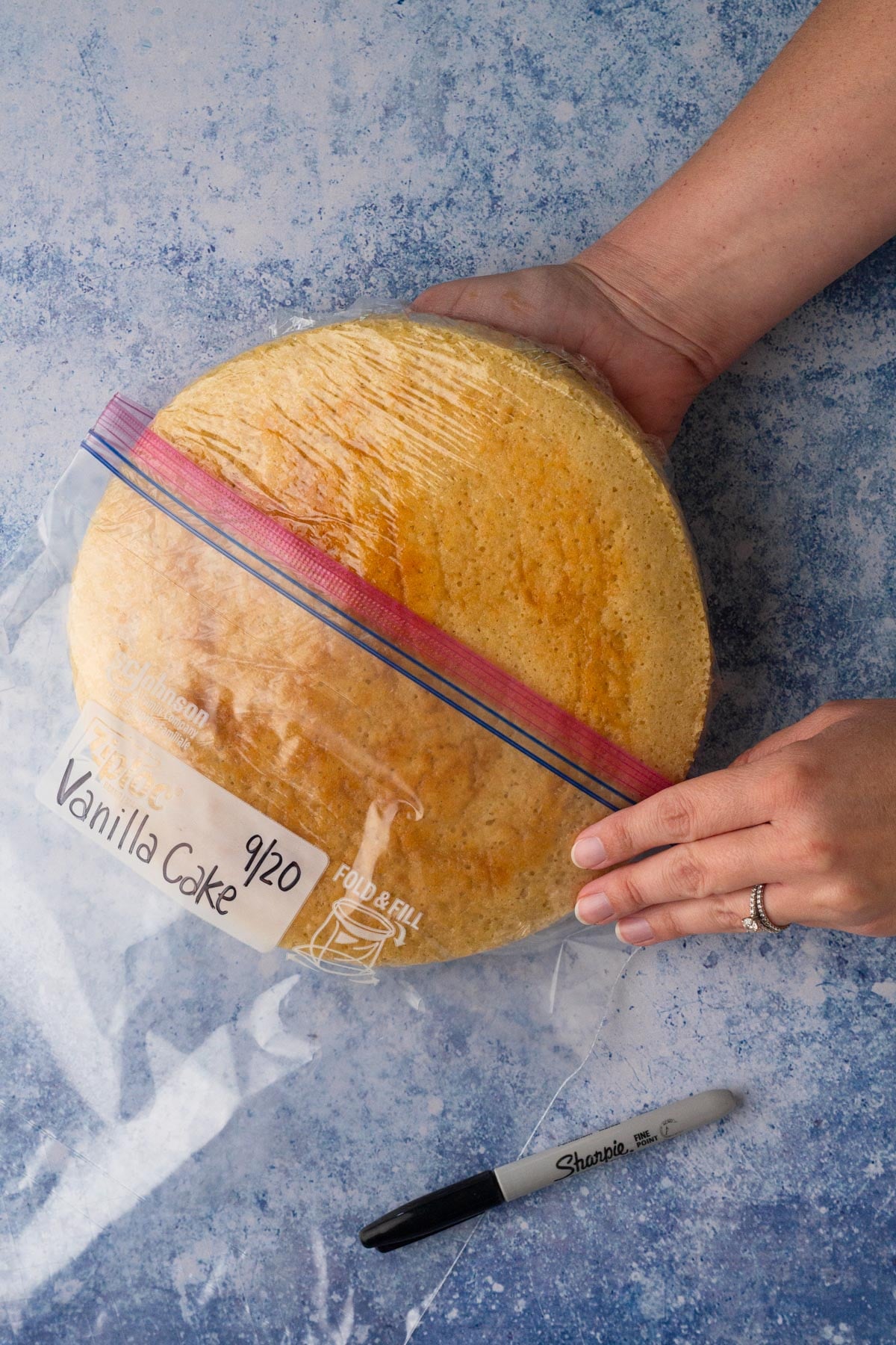 Hands placing a wrapped vanilla cake layer into a plastic bag.