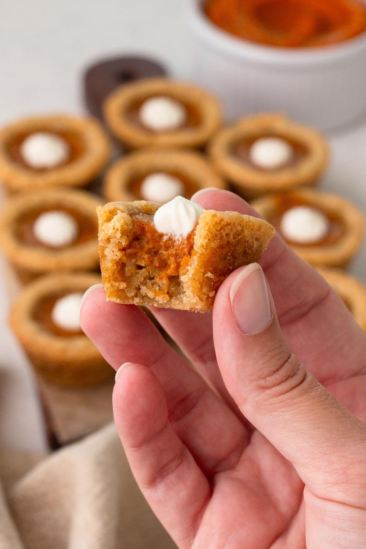 Hand holding a bitten sugar cookie cup with pumpkin pie filling and whipped cream.