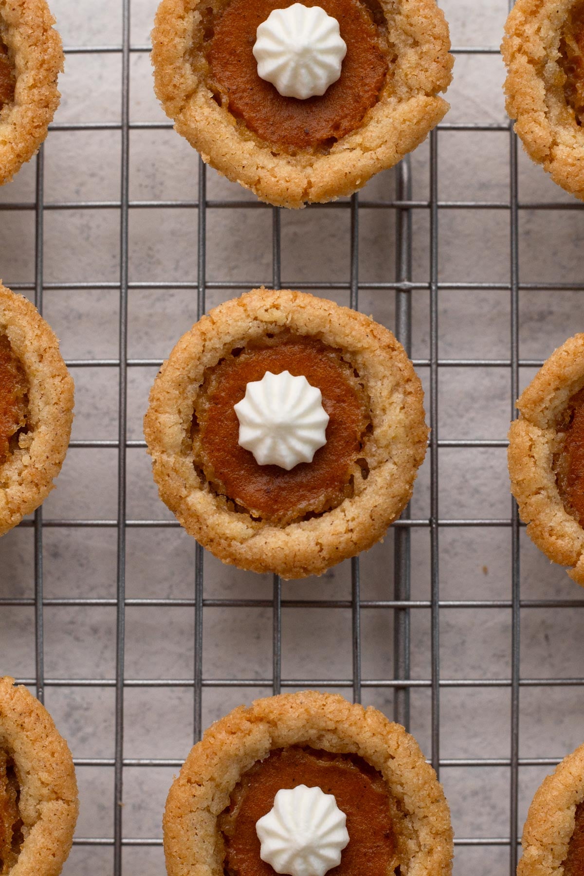 Cookie cups on a wire cooling rack with dollops of whipped cream topping piped on top.