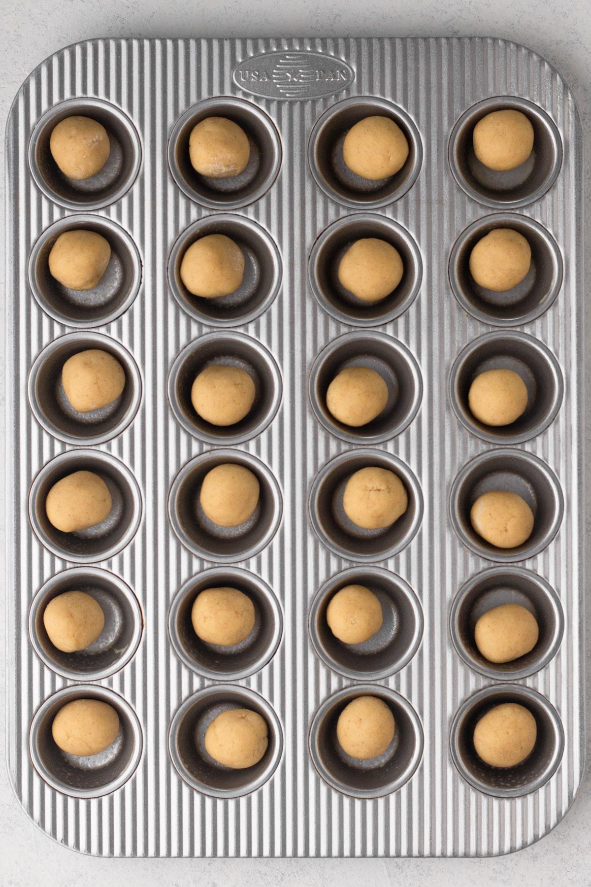 Balls of sugar cookie dough in the wells of a mini muffin pan.