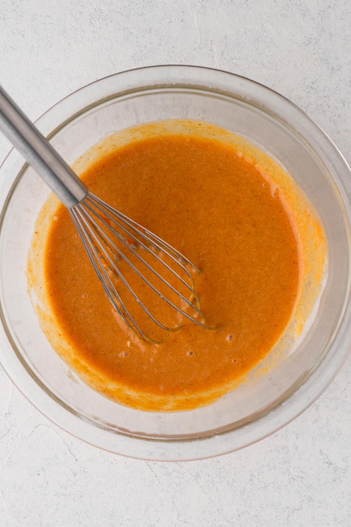 Pumpkin pie filling in a glass mixing bowl with a metal whisk.