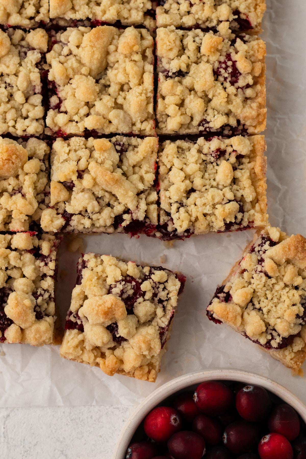 Overhead view of cranberry shortbread squares on a piece of parchment with a bowl of cranberries.