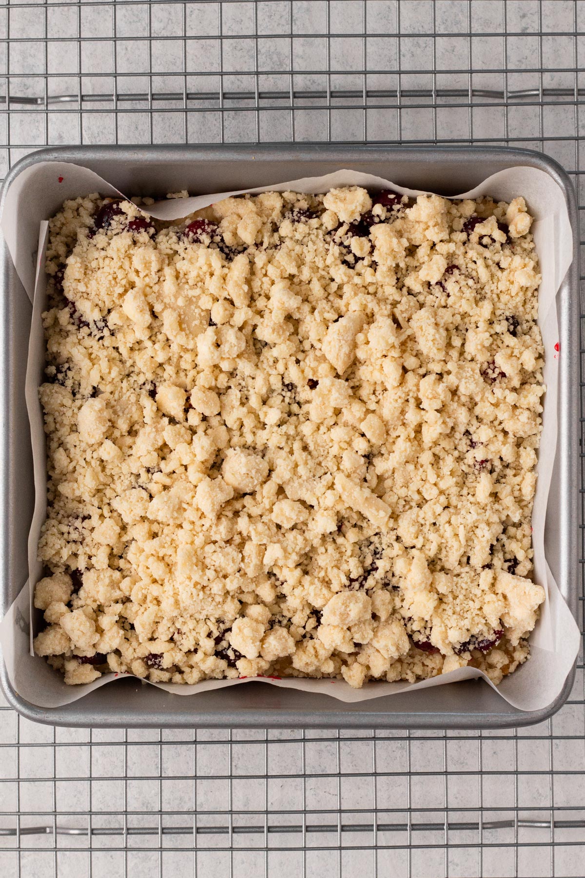 Par-baked crust topped with cranberry filling and shortbread crumb topping in a square metal pan.