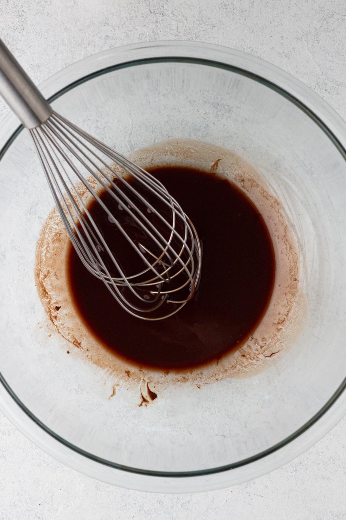 Melted butter and chocolate in a glass mixing bowl with a metal whisk.