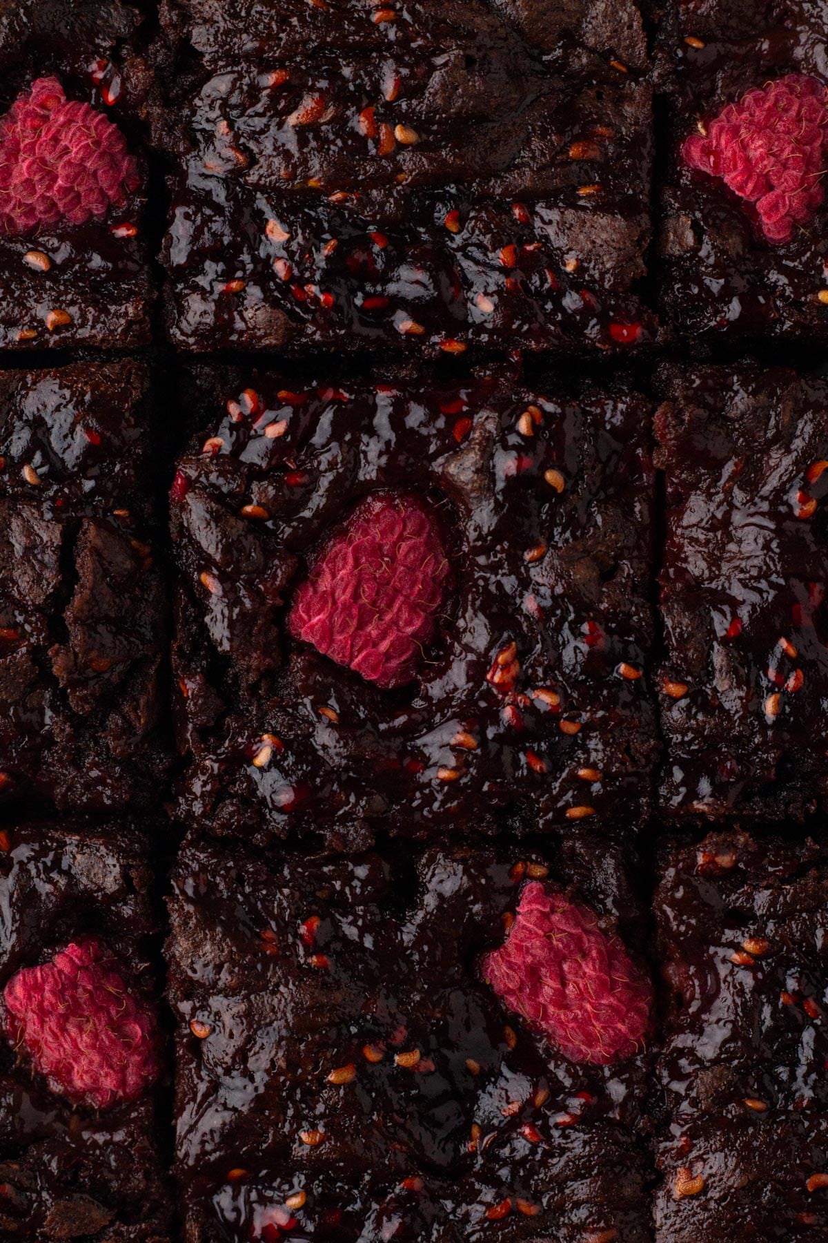 Overhead view of chocolate brownies with a raspberry jam swirl and fresh raspberries.