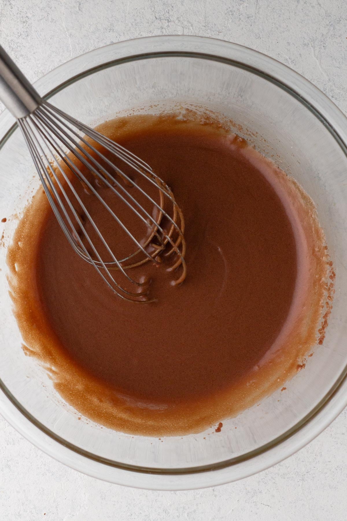 Wet ingredients blended together in a glass mixing bowl with a metal whisk.