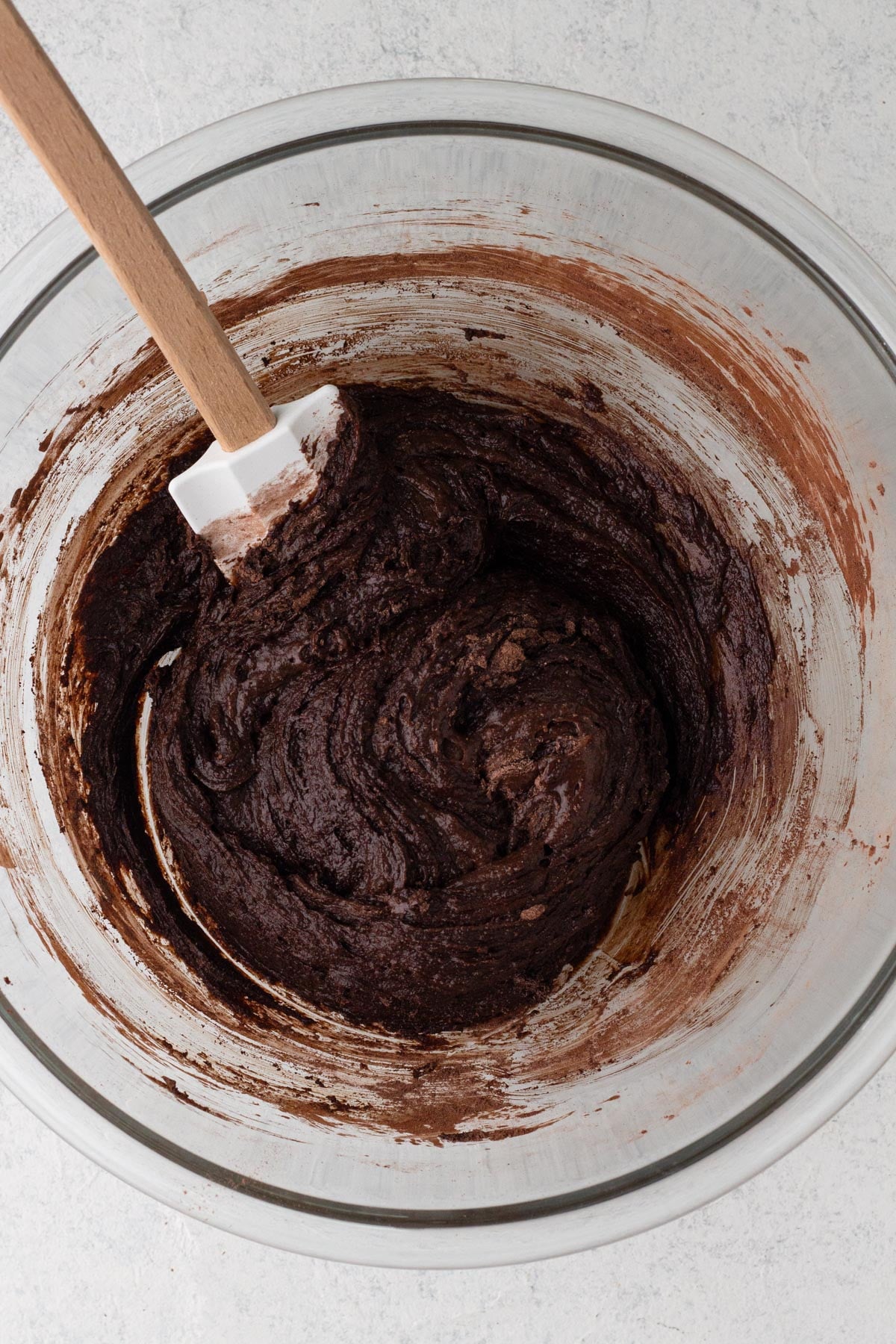 Brownie batter in a glass mixing bowl with a rubber spatula.