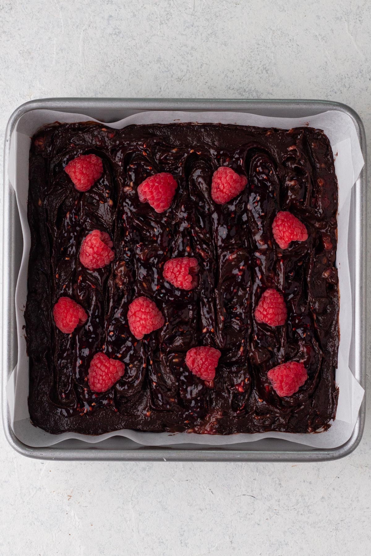 Brownie batter with fresh raspberries in a square baking pan.